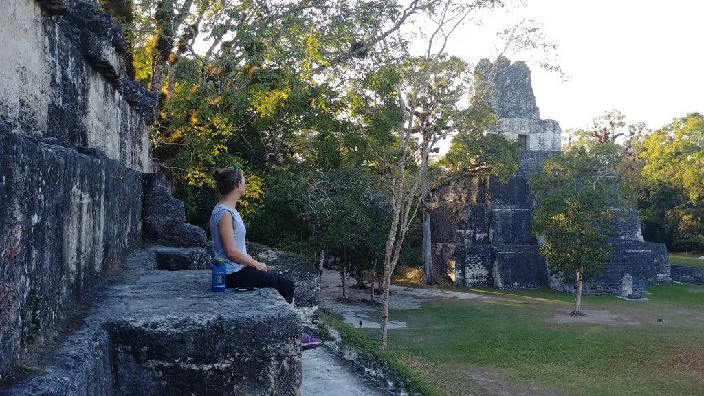 girl sitting on a stone wall in front of the main plaza in Tikal National Park