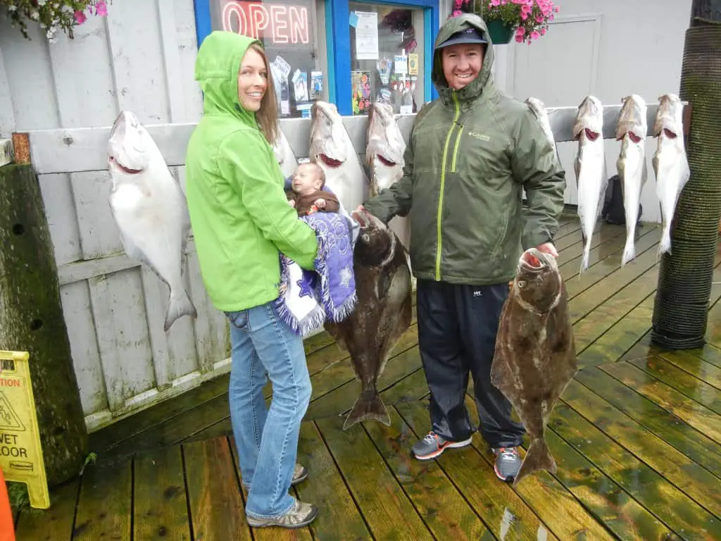 Man holding two Halibut he caught and woman holding baby. The Halibut are twice the size of the baby.