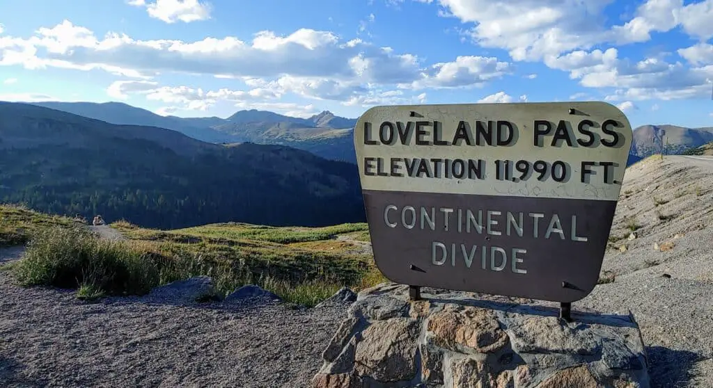 Sign that says Loveland Pass Elevation 11,990 ft Continental Divide with the Colorado Rocky Mountains in the summer time in the background