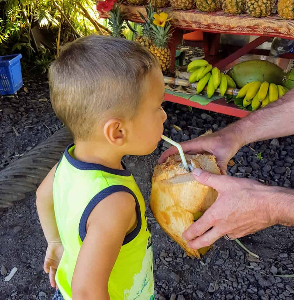 young boy drinking out of a coconut at a fruit stand in hawaii