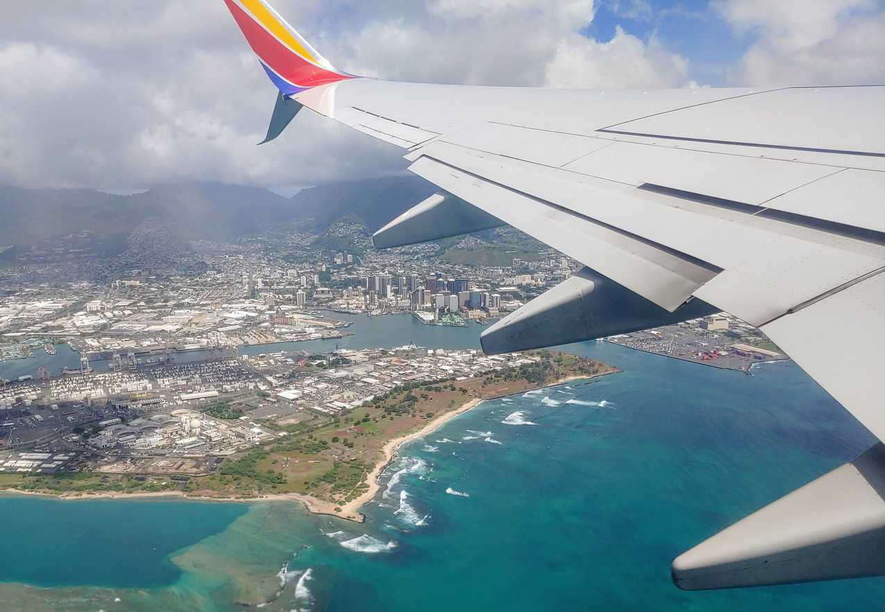 wing of a plane overlooking Hawaii - Family Travel On A Budget
