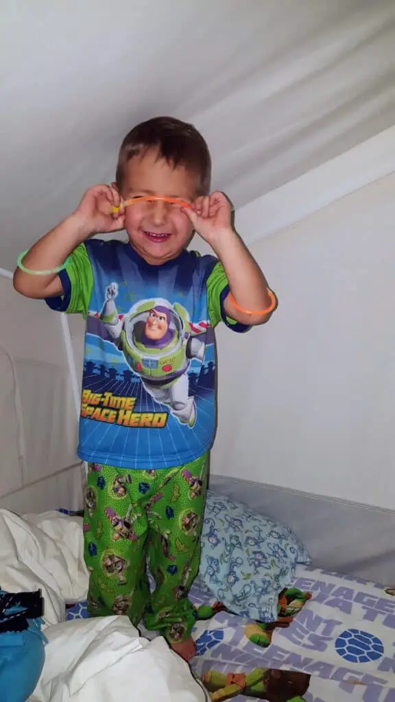 boy standing on his bed in a camper playing with glow sticks