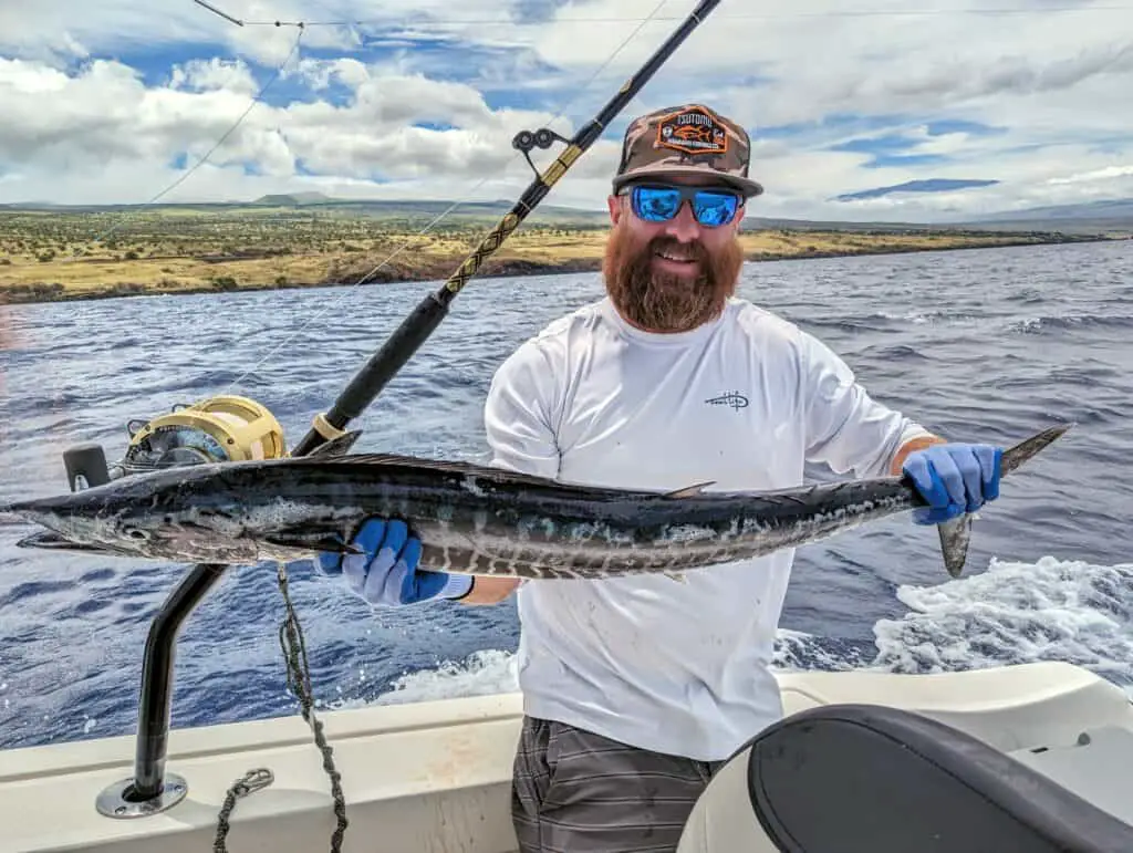 fisherman holding an ono he caught on a boat