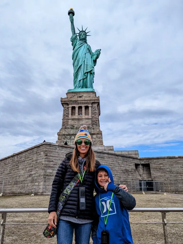 mom and son standing in front of the Statue of Liberty in New York